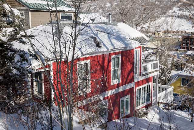 A red and white two-story house covered in snow, with bare trees around it.