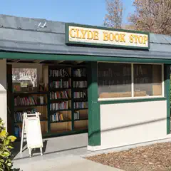 A small green and white building with a sign reading 'Clyde Book Stop' has a window filled with books on shelves.