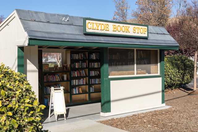 A small green and white building with a sign reading 'Clyde Book Stop' has a window filled with books on shelves.