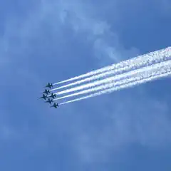 Six jet planes flying in formation against blue sky, leaving contrails in their wake.