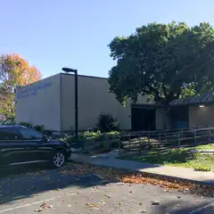 A car parked next to a tree and building with a sign that reads "Peralta Community College District".