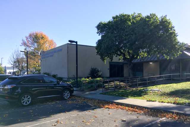 A car parked next to a tree and building with a sign that reads "Peralta Community College District".