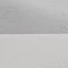 A flat, barren landscape of white sand with gentle undulations and a few small indentations.