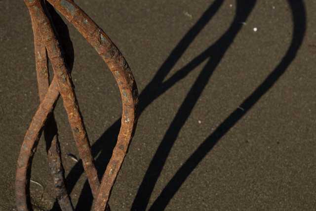 A collection of rusted metal rods casts long shadows on dark sand.