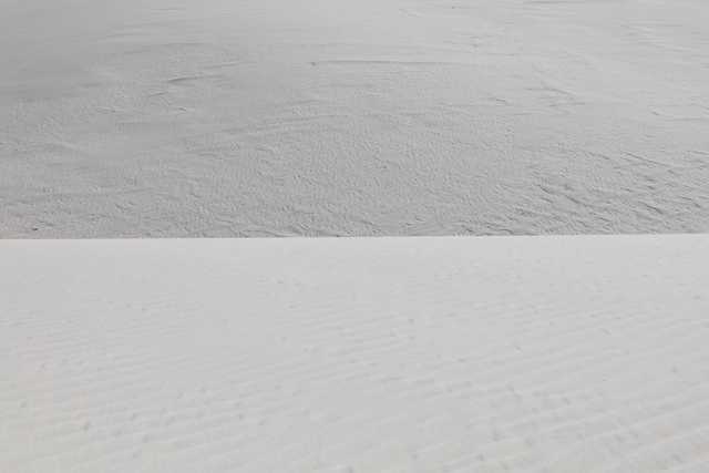 A flat, barren landscape of white sand with gentle undulations and a few small indentations.