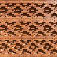 An orange brick wall features a pattern of cutouts that cast shadows on its surface.