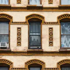 Three stories of a brick building with arched windows, decorative brown trim, and vertical ornamental panels between the windows.
