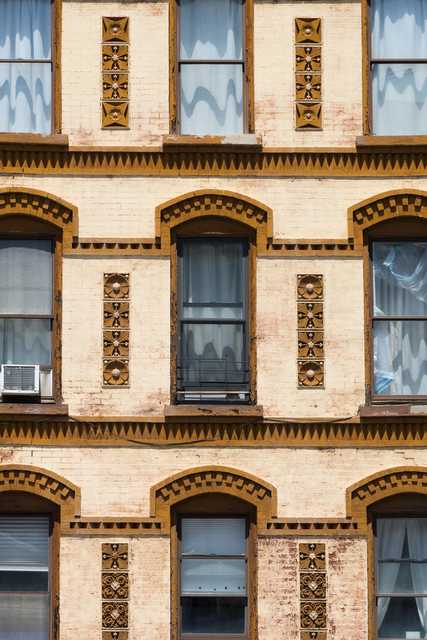 Three stories of a brick building with arched windows, decorative brown trim, and vertical ornamental panels between the windows.