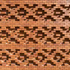 An orange brick wall features a pattern of cutouts that cast shadows on its surface.