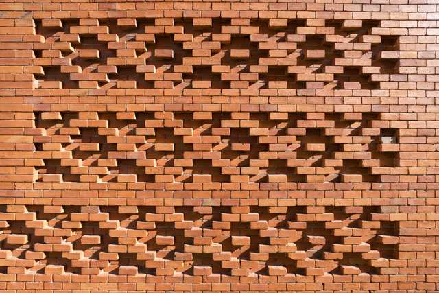 An orange brick wall features a pattern of cutouts that cast shadows on its surface.