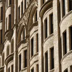 A close-up of a brick building facade featuring arched windows, decorative stone carvings, and curved bay sections.