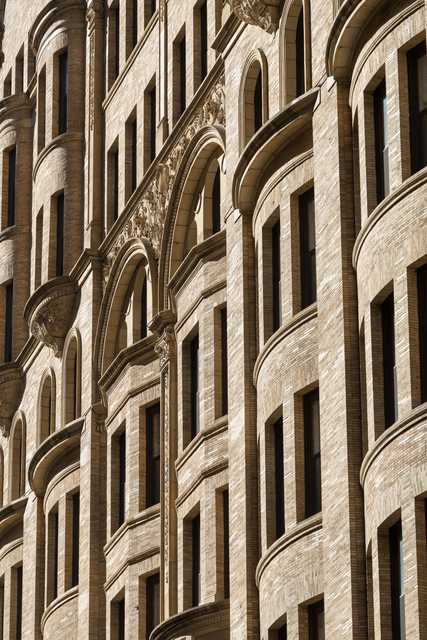 A close-up of a brick building facade featuring arched windows, decorative stone carvings, and curved bay sections.