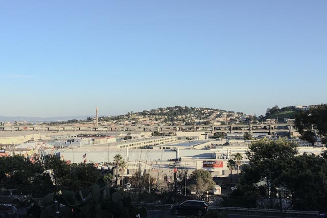 A large commercial district extends to a residential hillside under a clear blue sky.