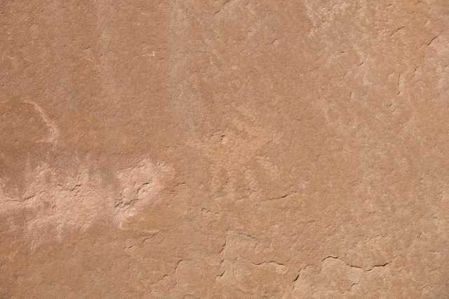 A flat, brown sandstone surface with a faint petroglyph of an antelope.