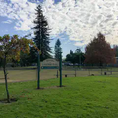 A sign for Lakeside Park stands on a grassy area with trees and a building in the background under a partly cloudy sky.