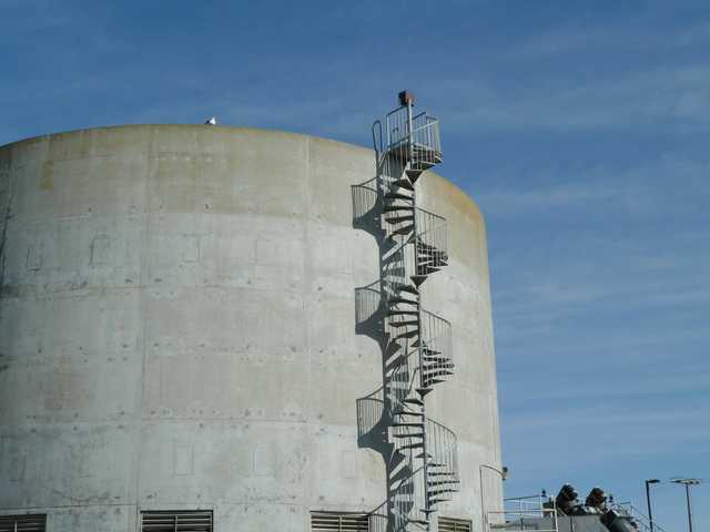 A metal spiral staircase with a railing is attached to the side of a large, cylindrical concrete structure.