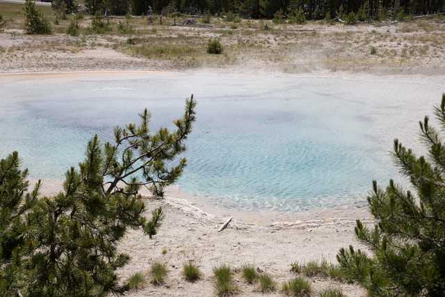 An aquamarine pool is surrounded by white sand and low green vegetation.