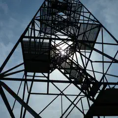 A tall metal structure with a spiral staircase leading to an observation deck, set against a partly cloudy sky.