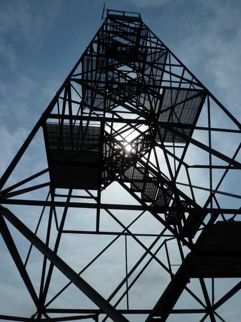 A tall metal structure with a spiral staircase leading to an observation deck, set against a partly cloudy sky.