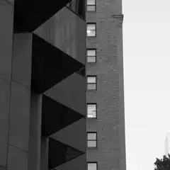 A tall building with many windows and a brick facade, partially obscured by another structure.