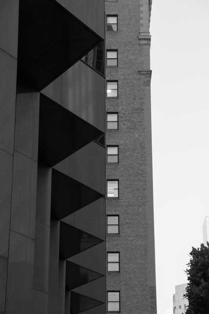 A tall building with many windows and a brick facade, partially obscured by another structure.