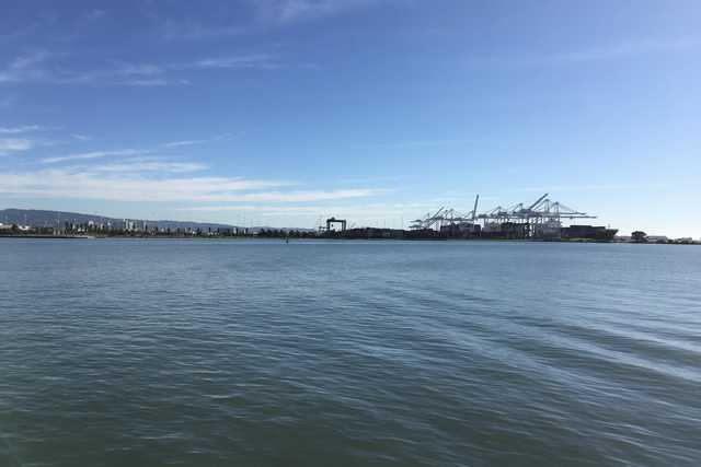 A waterway extends toward a waterfront industrial area with large container cranes and buildings in the distance.