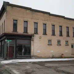 A two-story brick building with a storefront occupies a corner lot on a street covered in snow.