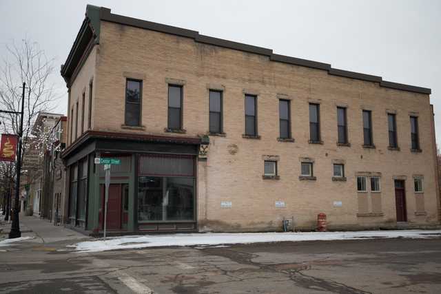 A two-story brick building with a storefront occupies a corner lot on a street covered in snow.