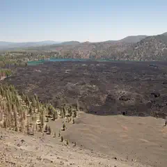 A dark lava field extends from a forest to a pair of blue lakes, with distant hills on the horizon.