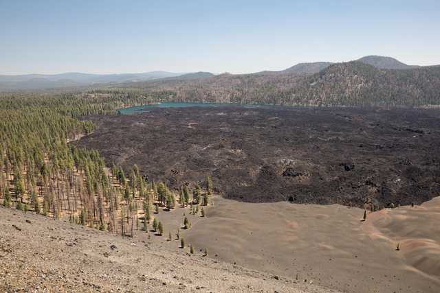 A dark lava field extends from a forest to a pair of blue lakes, with distant hills on the horizon.