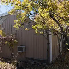 A small brown building with white trim is surrounded by trees with yellow leaves.