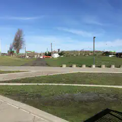 An asphalt path runs through a grassy area with concrete barriers along its edges.