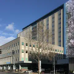 A large building with many windows and a flat roof, situated next to another building with reflective panels on its facade.