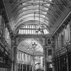 A covered market corridor features ornate ironwork, arched glass roofs, and hanging lanterns lining both sides of a central walkway.