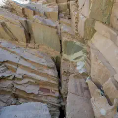 A sandstone canyon displays layered rock formations and red pictograph figures on a wall.