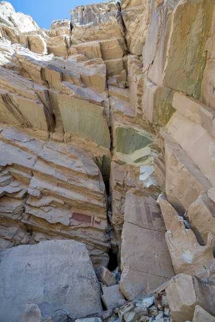 A sandstone canyon displays layered rock formations and red pictograph figures on a wall.