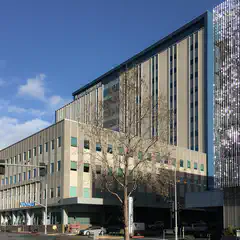 A large building with many windows and a flat roof, situated next to another building with reflective panels on its facade.