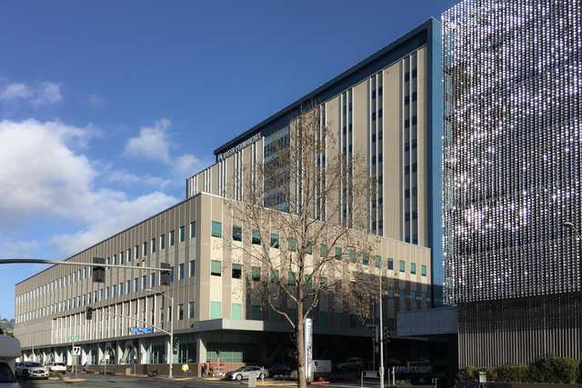 A large building with many windows and a flat roof, situated next to another building with reflective panels on its facade.