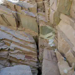 A sandstone canyon displays layered rock formations and red pictograph figures on a wall.