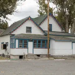 An old white house with blue trim and red accents has a small porch with steps leading up to it.