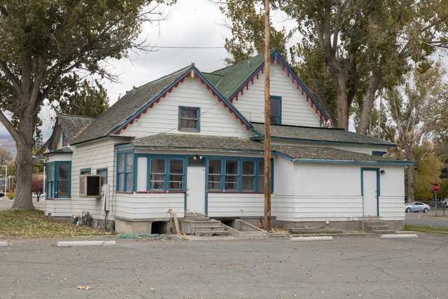 An old white house with blue trim and red accents has a small porch with steps leading up to it.