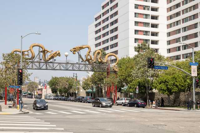 An ornate gateway depicting golden dragons spans a city street lined with vehicles and multi-story buildings.