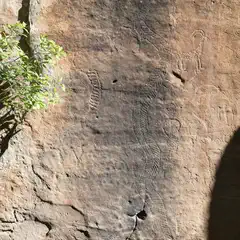 A rock face features several petroglyphs, including a human figure and an animal.
