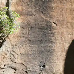 A rock face features several petroglyphs, including a human figure and an animal.