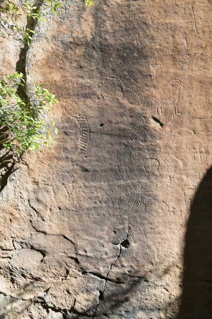 A rock face features several petroglyphs, including a human figure and an animal.