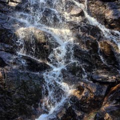 A small waterfall flows over dark, jagged rocks.