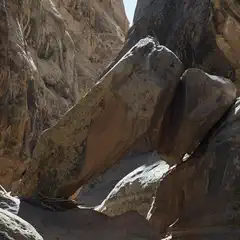 A narrow canyon contains large, angled rock formations and shadowed walls.