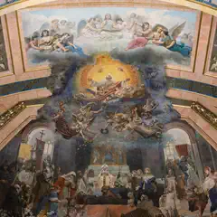 A grand ceiling fresco depicts a celestial scene with angels and divine figures above a gathering of robed figures in a richly decorated interior.