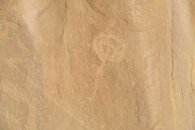 A tan rock wall displays a circular petroglyph.