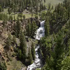 A waterfall cascading down a rocky mountain side into a stream surrounded by trees and rocks.